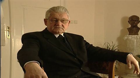 Mons. Vladimir Stanković sjedi u naslonjaču u sobi s bistom i biljkama, govori pred kamerom.
