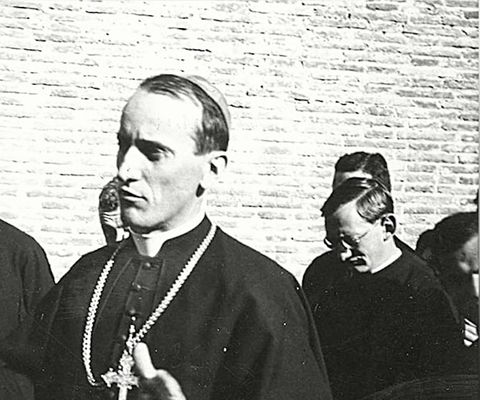 Nadbiskup Stepinac s pektoralnim križem među svećenicima, pred zidom od opeke.