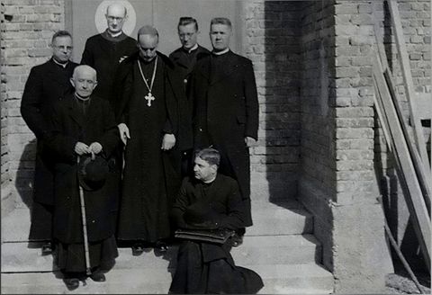 Skupna fotografija svećenika na stubama pred zidom od opeke; u sredini nadbiskup s pektoralnim križem.