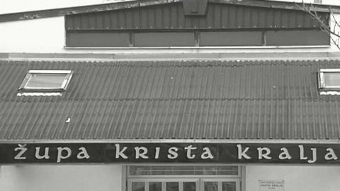 Natpis Župa Krista Kralja na pročelju niske zgrade s valovitim krovom.